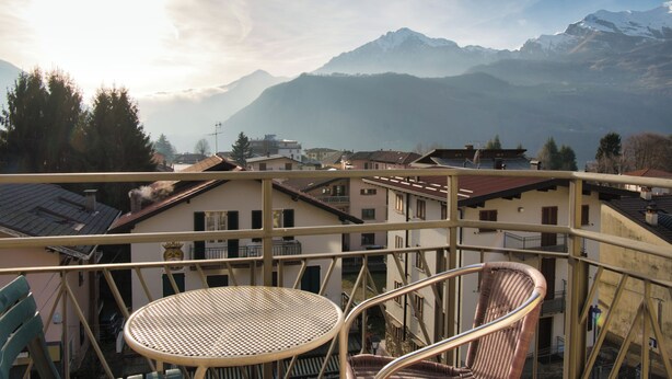 A balcony with a table and chairs overlooking a mountainous landscape with buildings in the foreground. - Garden - Pino Mugo - Two Bedroom Apartment, Sleeps 6 (Barzio)