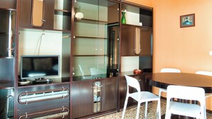 A room with a dining table, white chairs, a television on a cabinet, and a framed picture on the wall. - Garden - Pino Mugo - Two Bedroom Apartment, Sleeps 6 (Barzio)