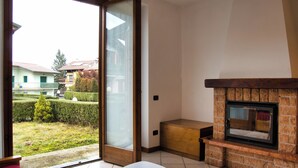 Una sala de estar moderna con chimenea, un ventanal corredero que da a un jardín y una mesita.