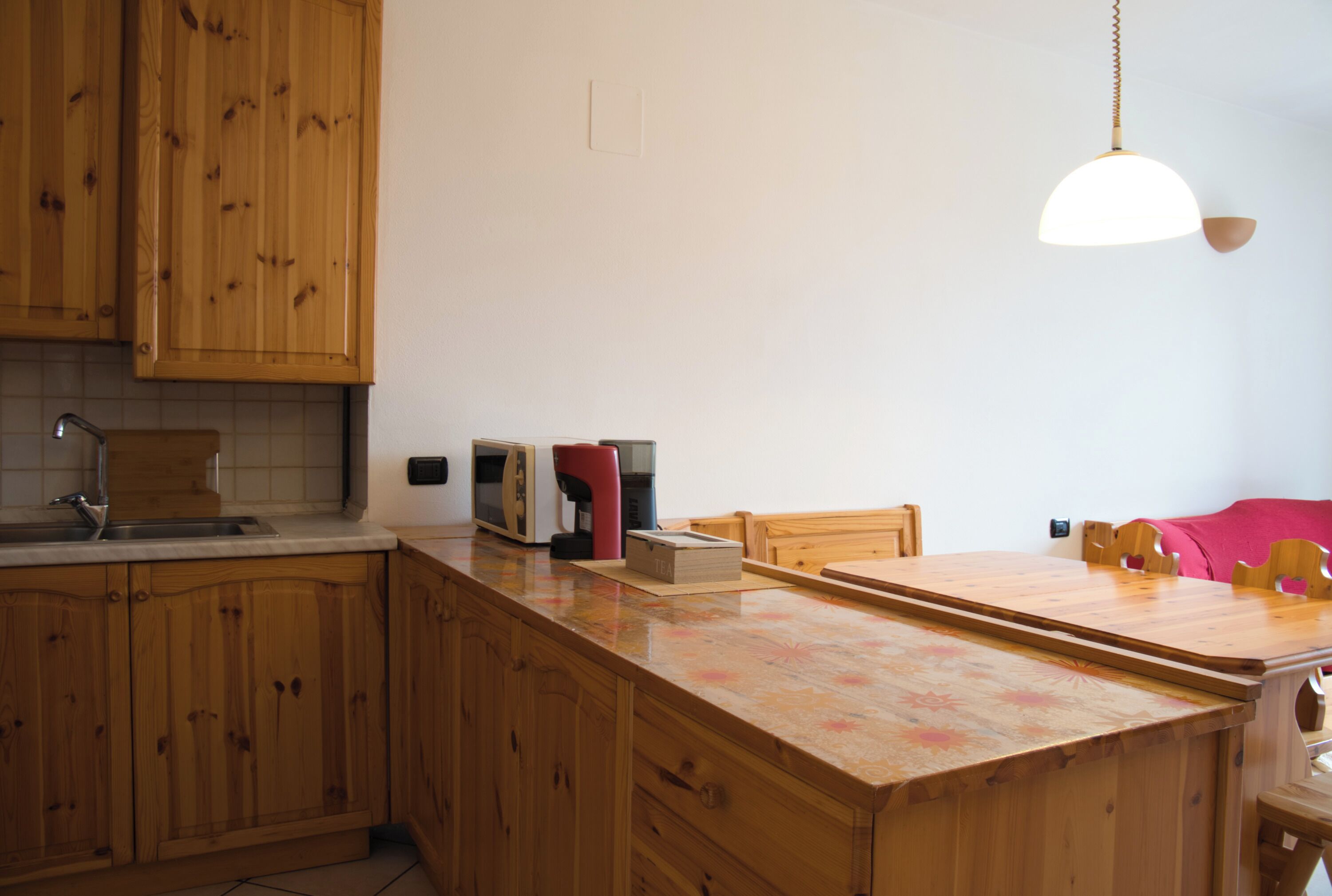 A kitchen with wooden cabinets, a countertop, a sink, a coffee maker, and a hanging light fixture.