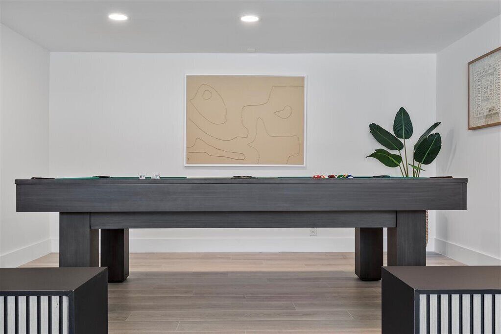 A billiards table in a room with a minimalist design, a framed abstract artwork on the wall, and a potted plant.