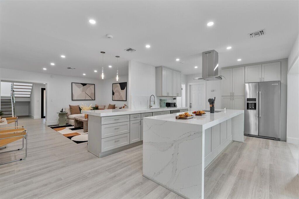 Une cuisine moderne avec des meubles blancs, un grand îlot central et des appareils électroménagers en acier inoxydable.