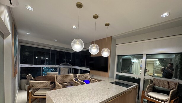 A modern kitchen with a central island, built-in appliances, and a dining area with wicker chairs. - Luxurious beachfront apartment in Itapema, SC. (Itapema)