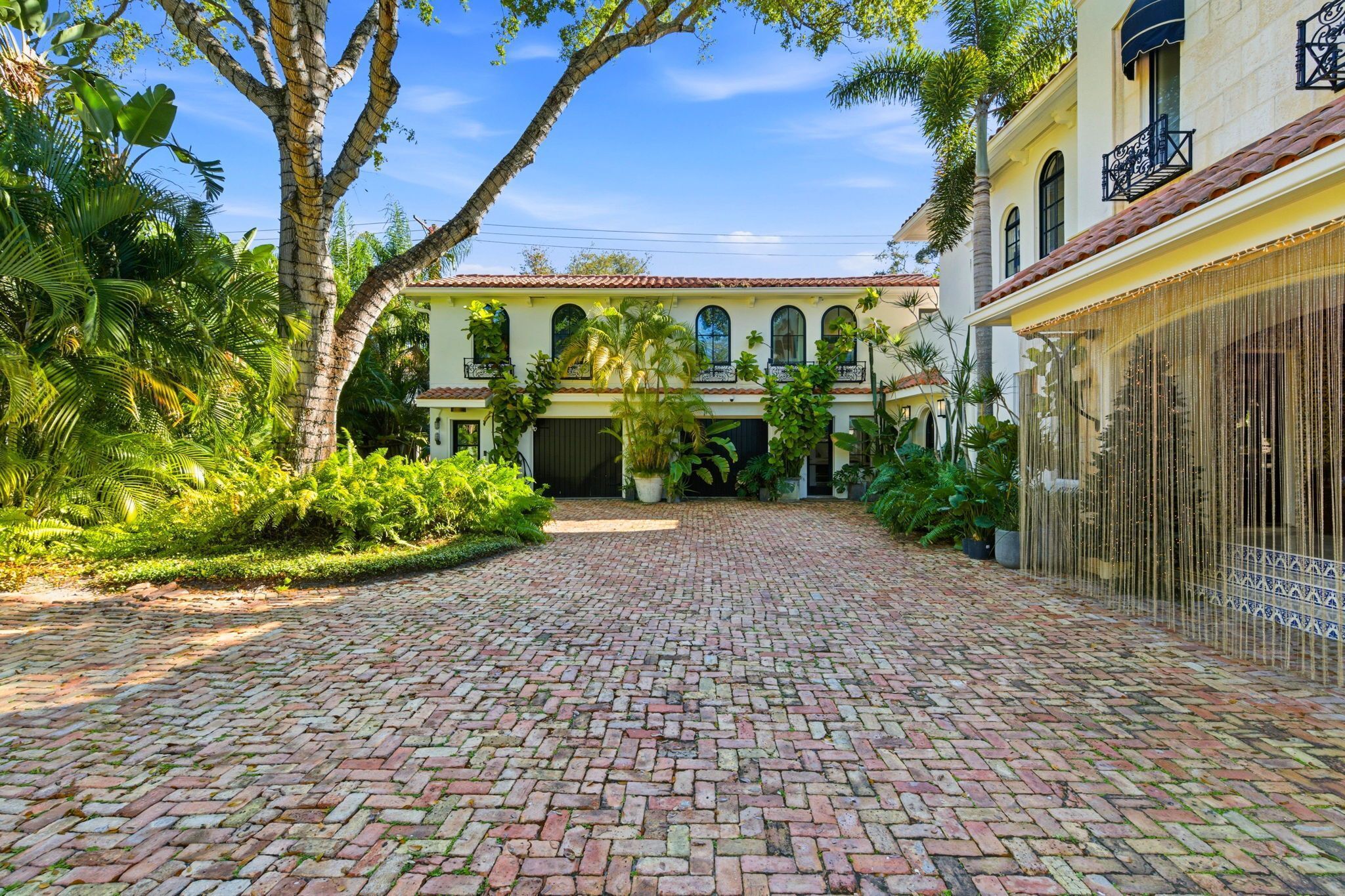 A courtyard with a paved walkway leading to a building with arched windows and a tiled roof.