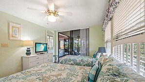 Ein Schlafzimmer mit zwei Betten, einem Fernseher, einem Deckenventilator und einem Balkon mit Vorhängen.