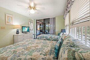A bedroom with two beds, a television, a ceiling fan, and a balcony with curtains. - Wild Pines B301 (Bonita Springs)