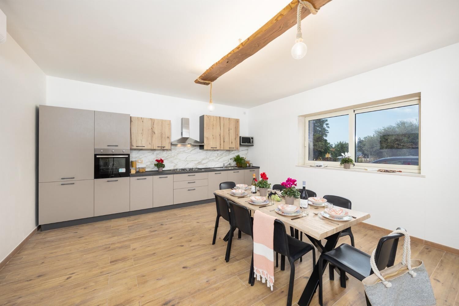A modern kitchen with wooden cabinets, a dining table set for four, and a window with a view of the outdoors.