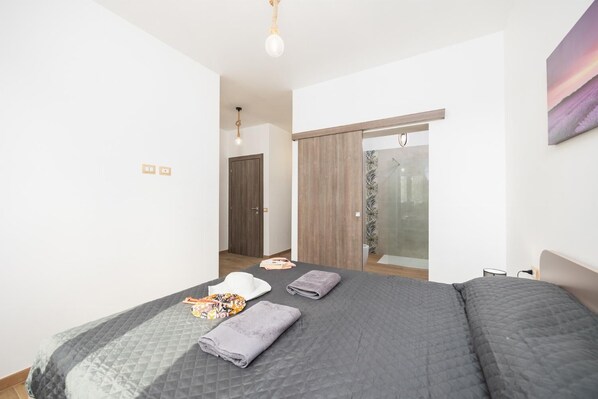 A bedroom with a bed, a bathroom with a shower, and a door leading to another room. - Villa Fenice - Five Bedroom Villa, Sleeps 10 (Scicli)