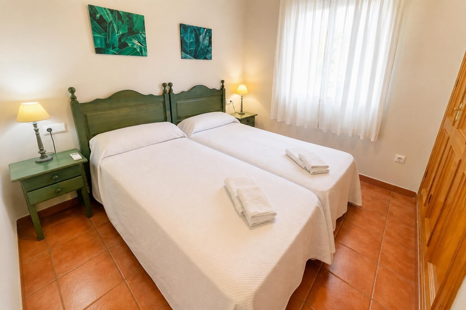 A double room with two beds, a nightstand with a lamp, and a window with curtains.