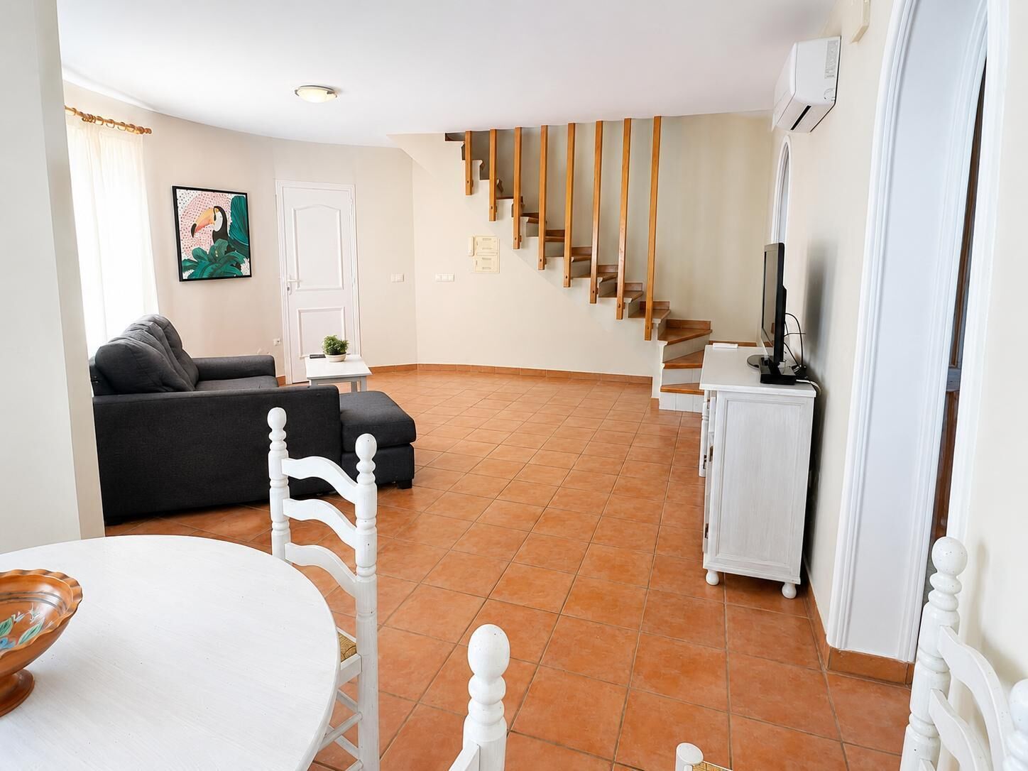 Una sala de estar con sofá, una mesa de comedor, una escalera y un televisor.