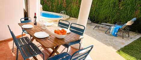 An outdoor dining area with a pool, chairs, and a table set for a meal.