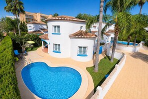 Un área junto a la piscina con una piscina en forma de corazón, un edificio blanco con detalles azules y palmeras.
