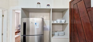 Eine kleine Küche mit einem Edelstahl-Kühlschrank, einer Ablage mit Gläsern und einem Schrank mit gestapelten Tellern.