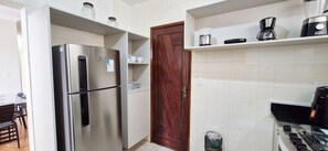 Eine kleine Küche mit einem Edelstahlkühlschrank, einer Holztür und einer Kaffeemaschine auf der Arbeitsplatte.