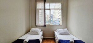 Ein kleines Zimmer mit zwei Betten, einem fensterbelagten Fenster und Blick auf Gebäude.