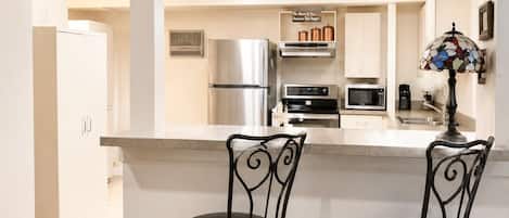 Eine Küche mit zwei schwarzen Metall-Barhocker, einem Kühlschrank, einer Mikrowelle, einem Backofen und einer Kaffeemaschine.