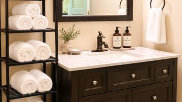 A bathroom with a dark wooden vanity, a mirror, a towel rack, and a shelf with neatly rolled towels.