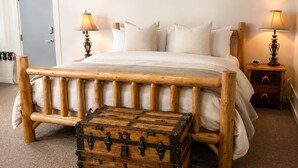 Ein Bett mit hölzernem Kopfteil und Fußteil, zwei Nachttischlampen, eine Holzkommode und eine Tür.