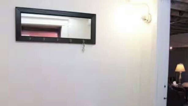 Eine weiße Bank mit orangefarbenem Sitzkissen in einem Raum mit weißer Wand und einem Spiegel darüber.