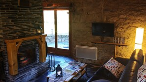 Ett mysigt vardagsrum med en öppen spis i sten, en platt-TV som är monterad på väggen och en bekväm soffa med mönstrade kuddar.