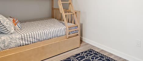 A bunk bed with a ladder, a patterned bedspread, and pillows. There are two wall-mounted artworks and a patterned rug on the floor.