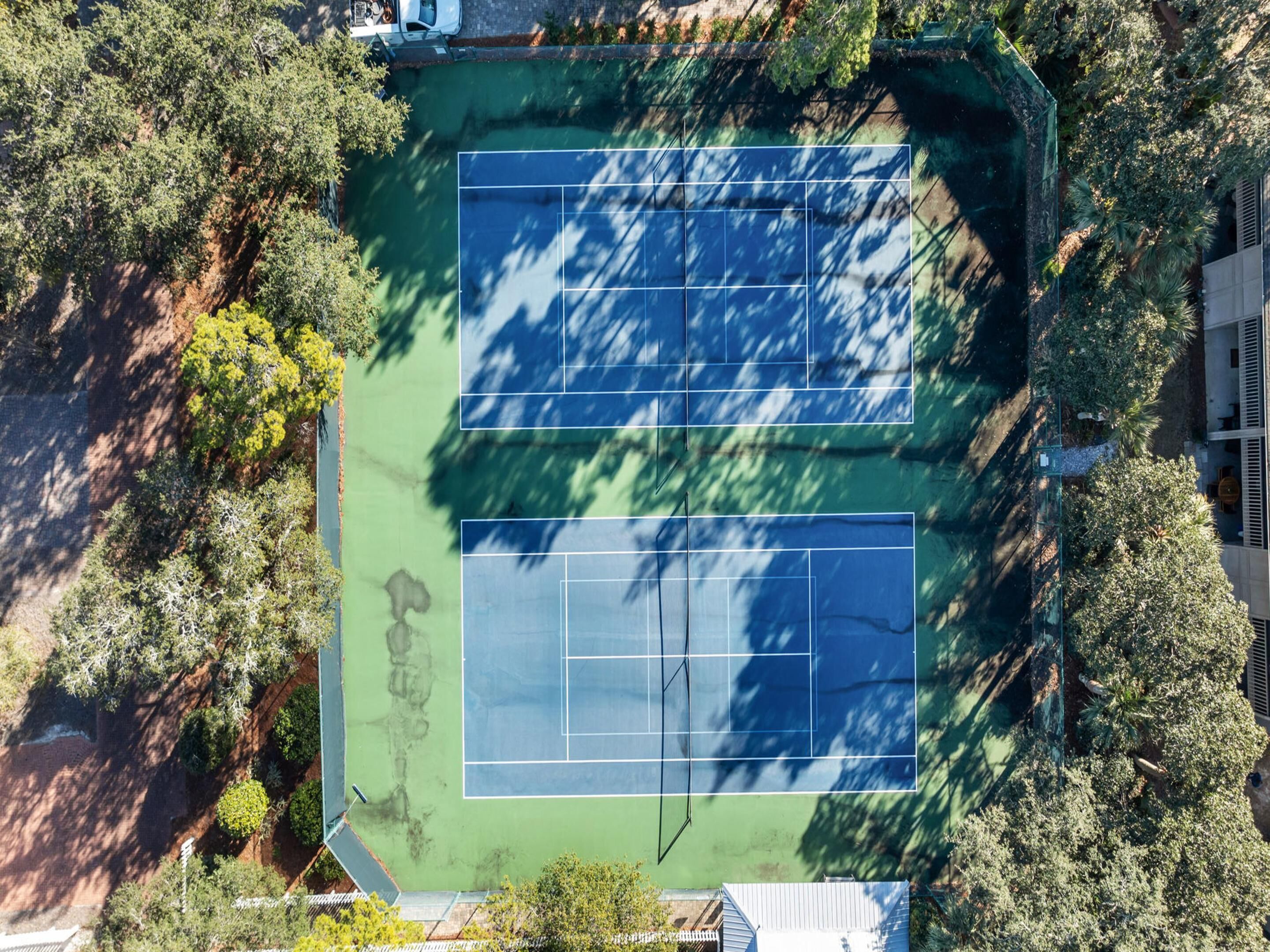 An aerial view of a tennis court surrounded by dense greenery.
