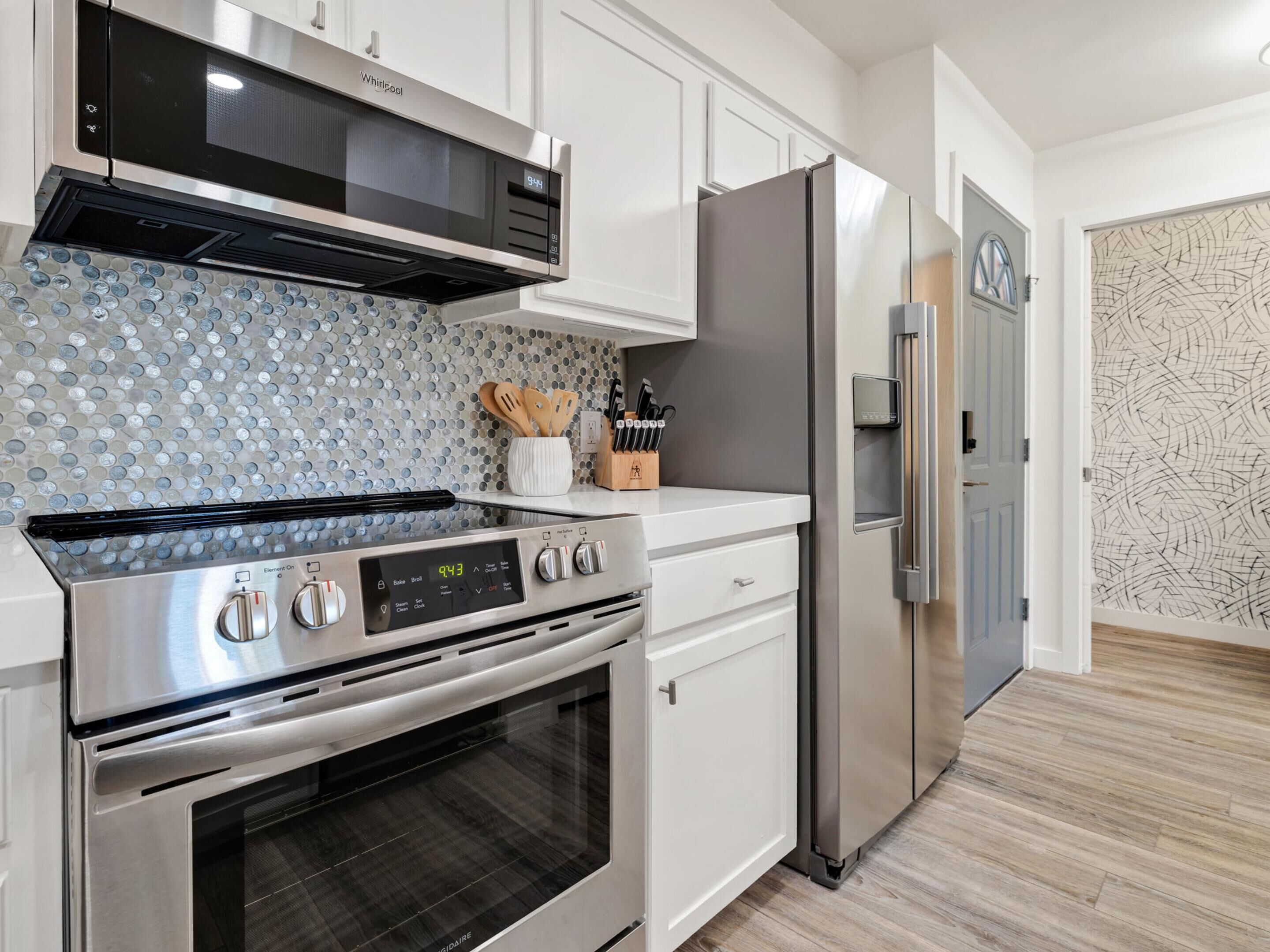 Eine moderne Küche mit Edelstahlkochfeld, Backofen und Kühlschrank, weißen Schränken und einer Spritzschutzwand mit kreisförmigem Muster.