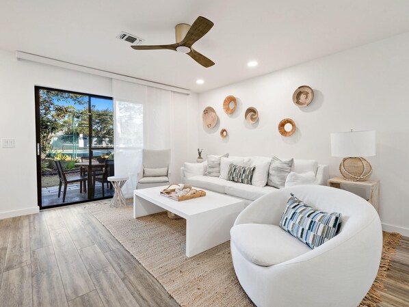 Una sala de estar moderna con un sofá blanco, un sillón blanco redondo, una mesa de centro y una zona de comedor con una mesa y sillas.
