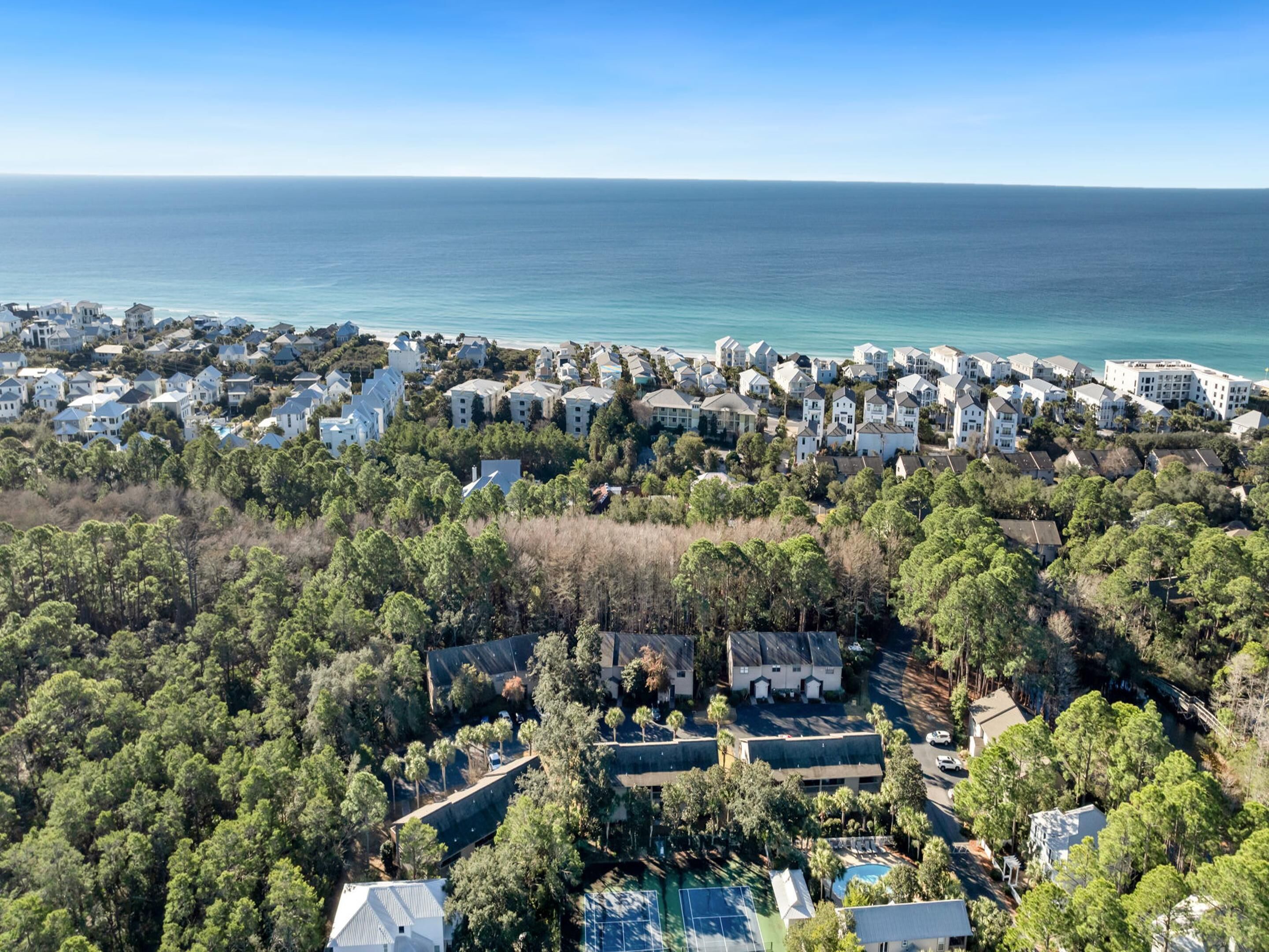 Vue aérienne d’un quartier résidentiel situé sur la côte, avec des maisons, une végétation luxuriante et une vue dégagée sur l’océan.