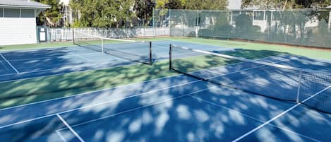 An outdoor tennis court with a net, surrounded by trees and a white fence.