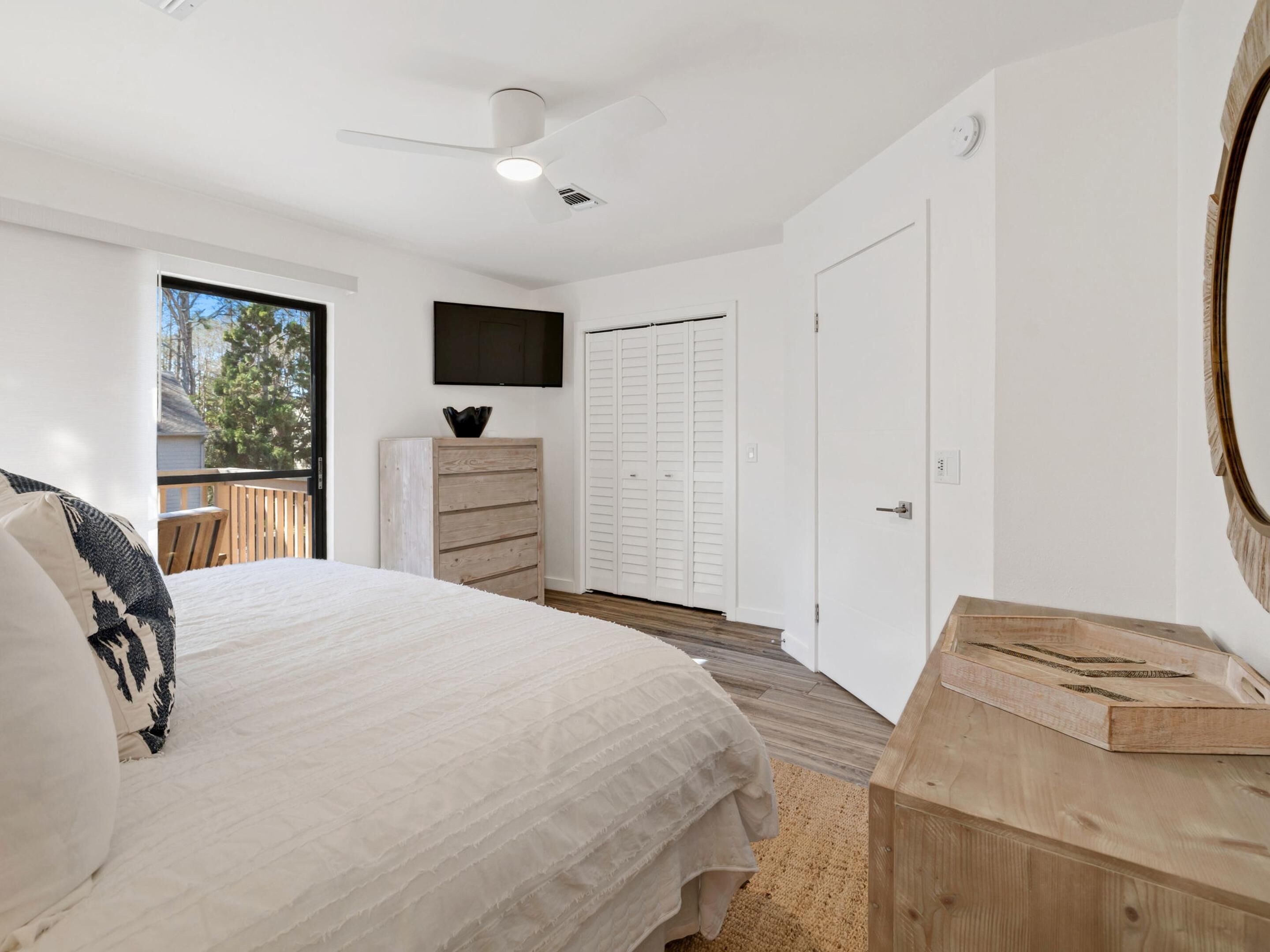 A bedroom with a bed, a dresser, a TV mounted on the wall, and a door leading to a balcony.