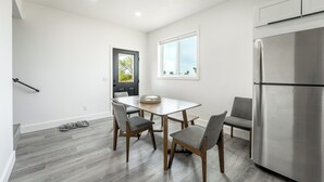 Une cuisine moderne équipée d’un réfrigérateur en acier inoxydable, d’une table à manger avec quatre chaises et d’une fenêtre donnant sur un paysage verdoyant.