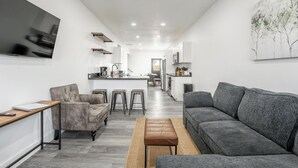 Un salon moderne avec un canapé gris, une table basse en bois et un téléviseur fixé au mur.