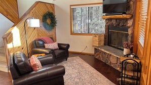 A cozy living room with a fireplace, leather sofa, and a stone accent wall. - Christmas Tree Retreat – Cozy Forest Getaway in Pinetop - Sleeps 8 (Pinetop Country Club)
