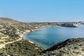 Paesaggio costiero con vista aperta sul mare, una strada sinuosa e vegetazione rada.