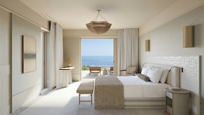 A bedroom with a large bed, a bedside table, a nightstand, a hanging light fixture, and a view of the sea. - Erema, a Member of Design Hotels (Milos)