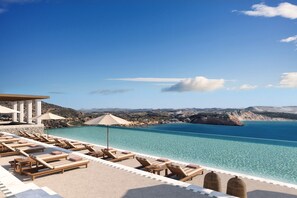 A poolside area with lounge chairs and umbrellas overlooking a clear blue sea and distant hills. - Erema, a Member of Design Hotels (Milos)