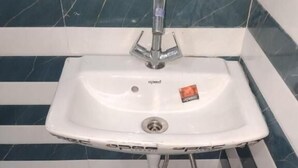 Un lavabo blanc, avec un seul robinet, installé devant un mur recouvert de carreaux aux rayures bleues et blanches.