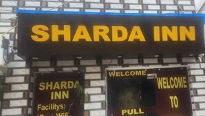 Une enseigne pour le Sharda Inn, avec une plaque directionnelle et une pancarte d’accueil.