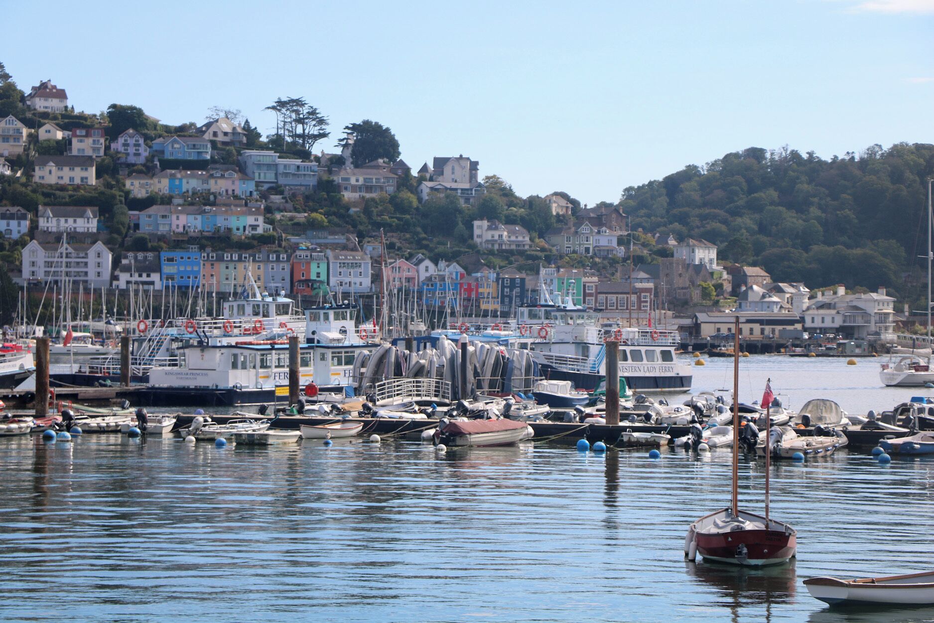 A harbor with numerous boats docked, a prominent red boat in the foreground, and colorful buildings in the background.