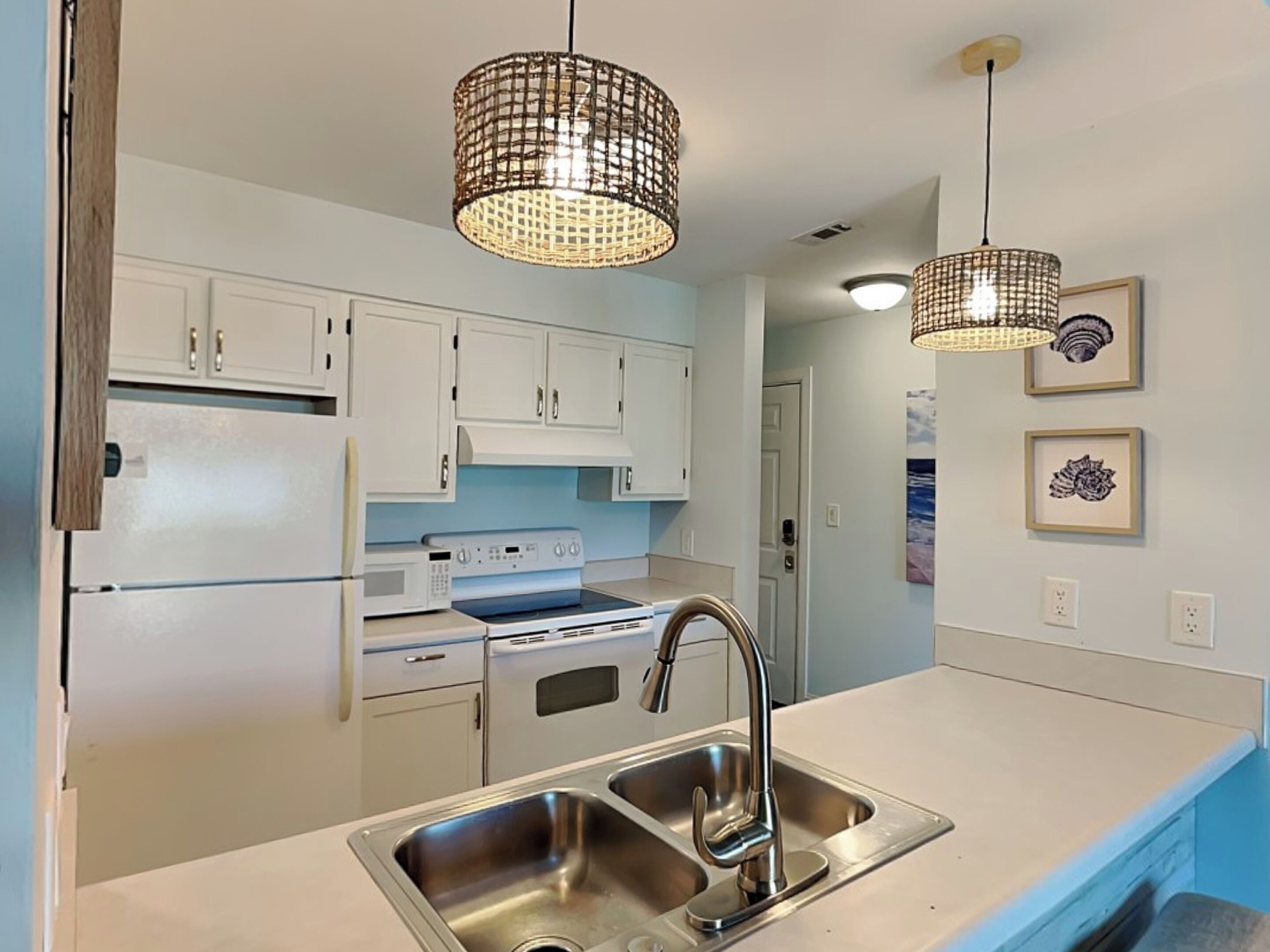 A modern kitchen with white cabinets, stainless steel appliances, and pendant lighting.