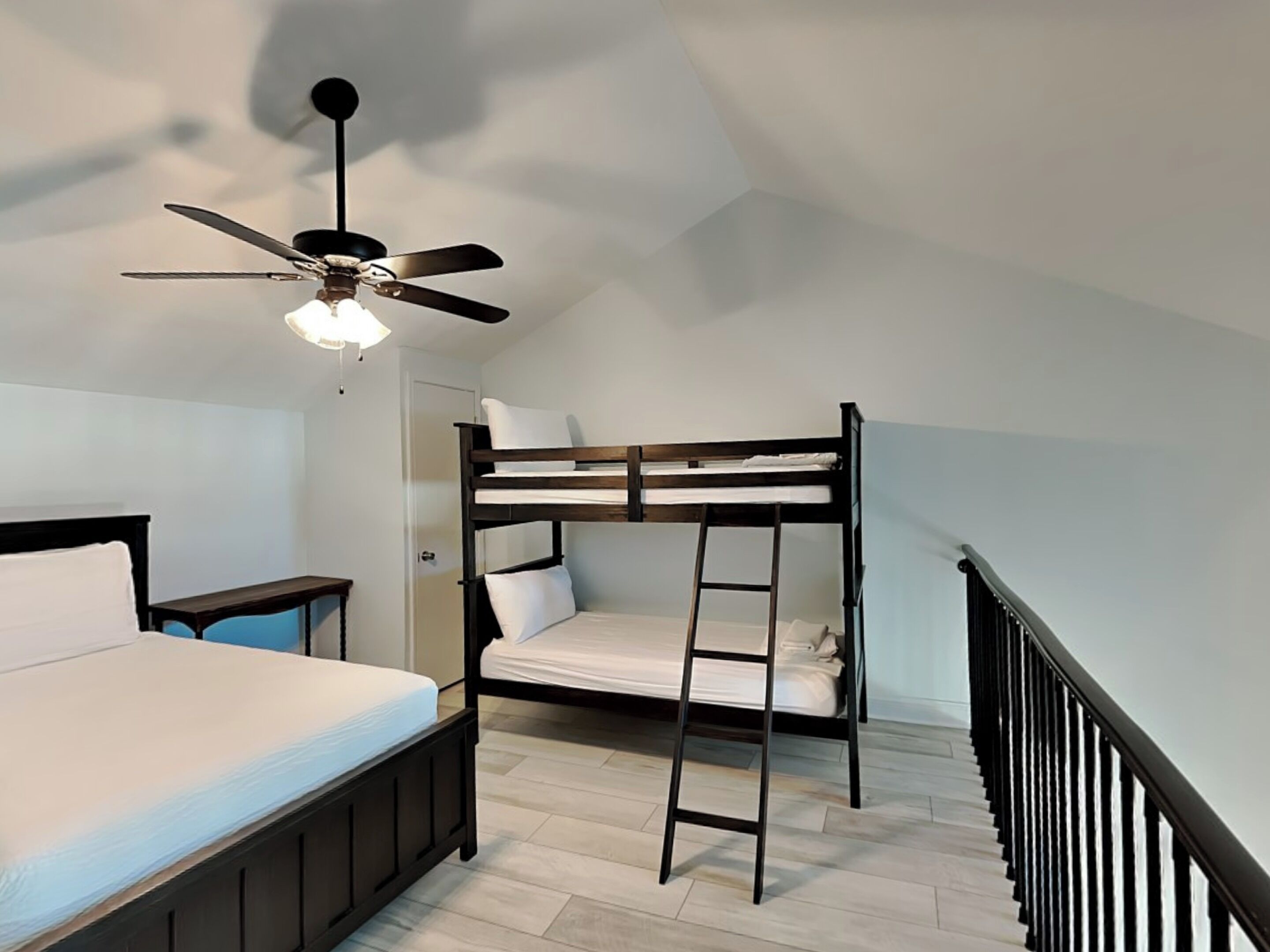 A room with a bunk bed, a desk, a chair, and a ceiling fan.