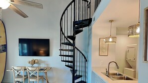 A modern kitchen with a built-in sink, a dining area with a wooden table and chairs, and a black spiral staircase. - Treasure Cove #d308 - Paradise City (Panama City Beach)