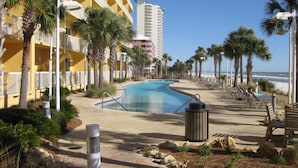 Area piscina con vista aperta sull'oceano, circondata da palme e un edificio giallo.
