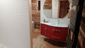 Une salle de bain avec des murs en bois, un meuble-lavabo blanc doté de tiroirs rouges, un grand miroir et un meuble noir.