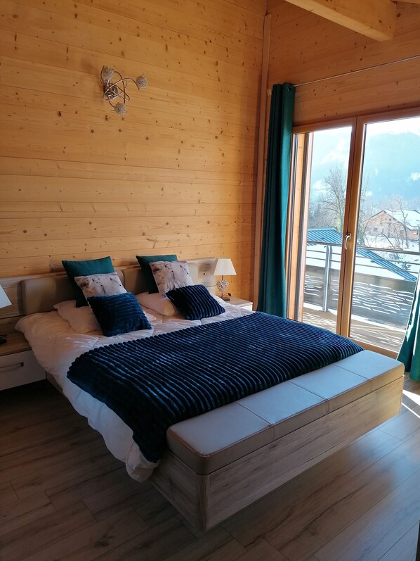 Ein Schlafzimmer mit Holzvertäfelung, einem großen Bett, zwei Nachttischen und Blick auf eine verschneite Landschaft durch ein Fenster.