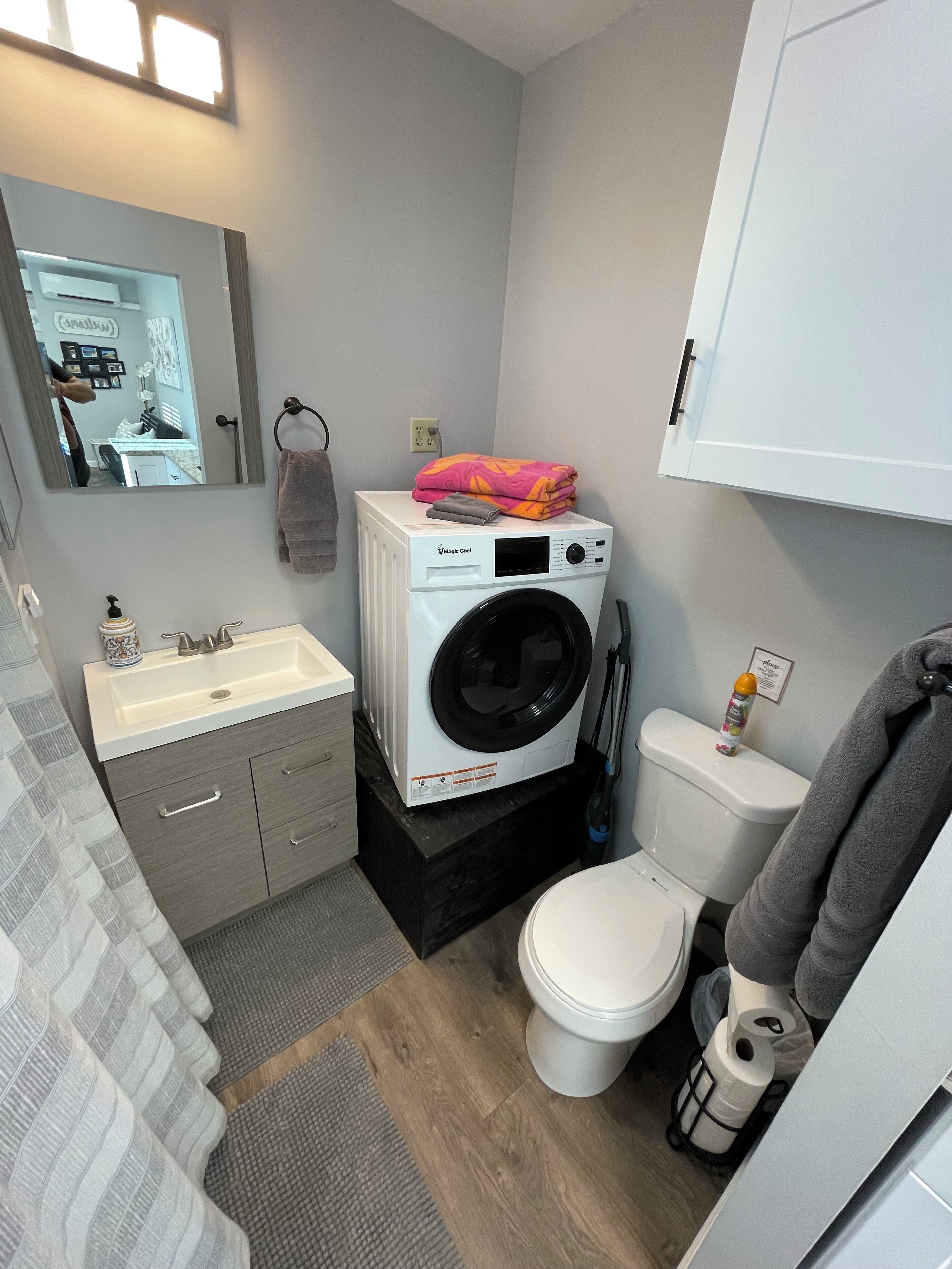 A compact bathroom with a washing machine, a toilet, a sink, and a mirror.