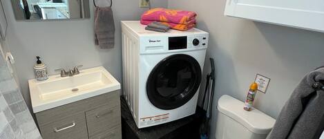 A compact bathroom with a washing machine, a toilet, a sink, and a mirror.