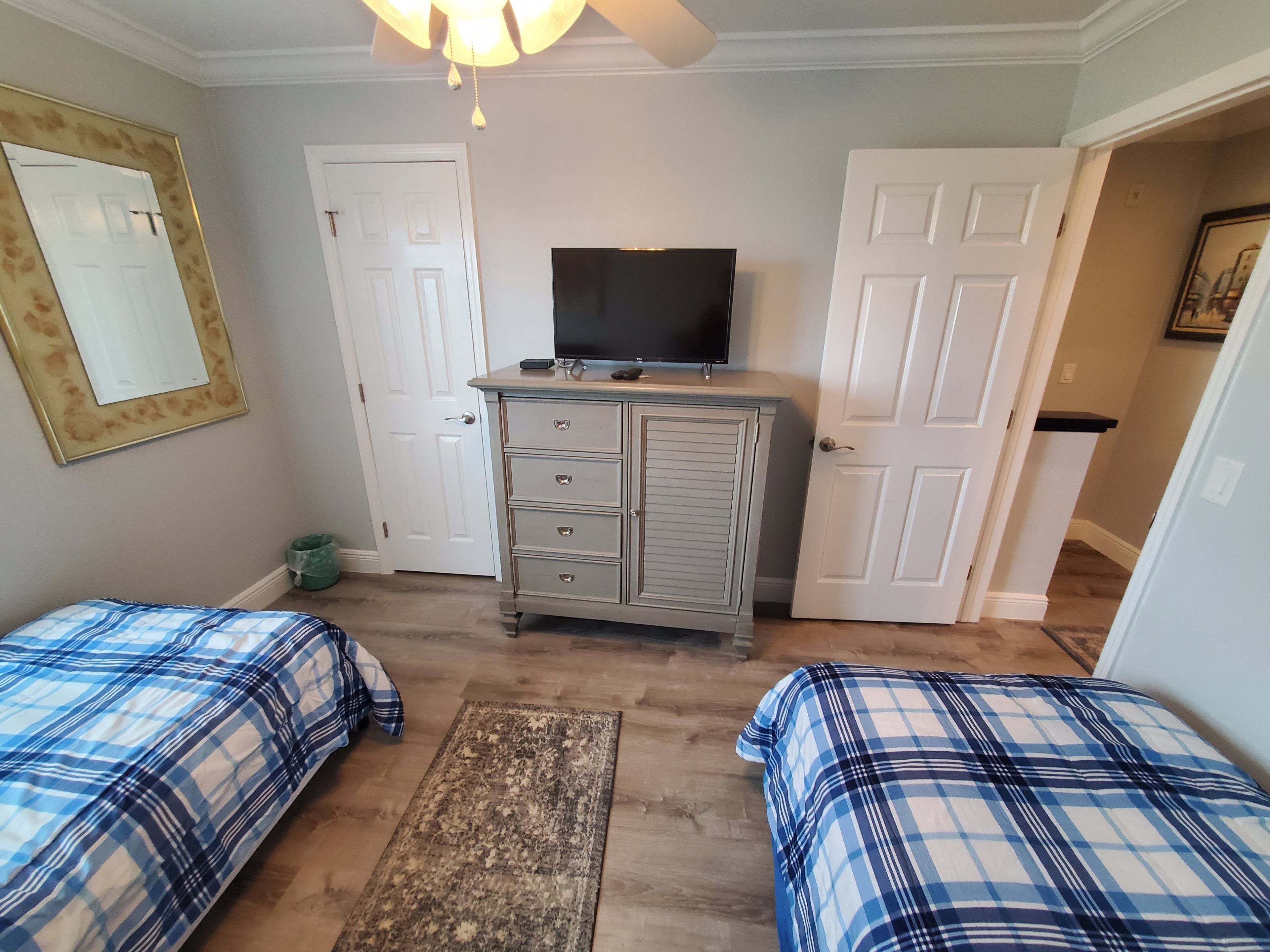 Une chambre avec deux lits, une commode, un téléviseur et une porte.