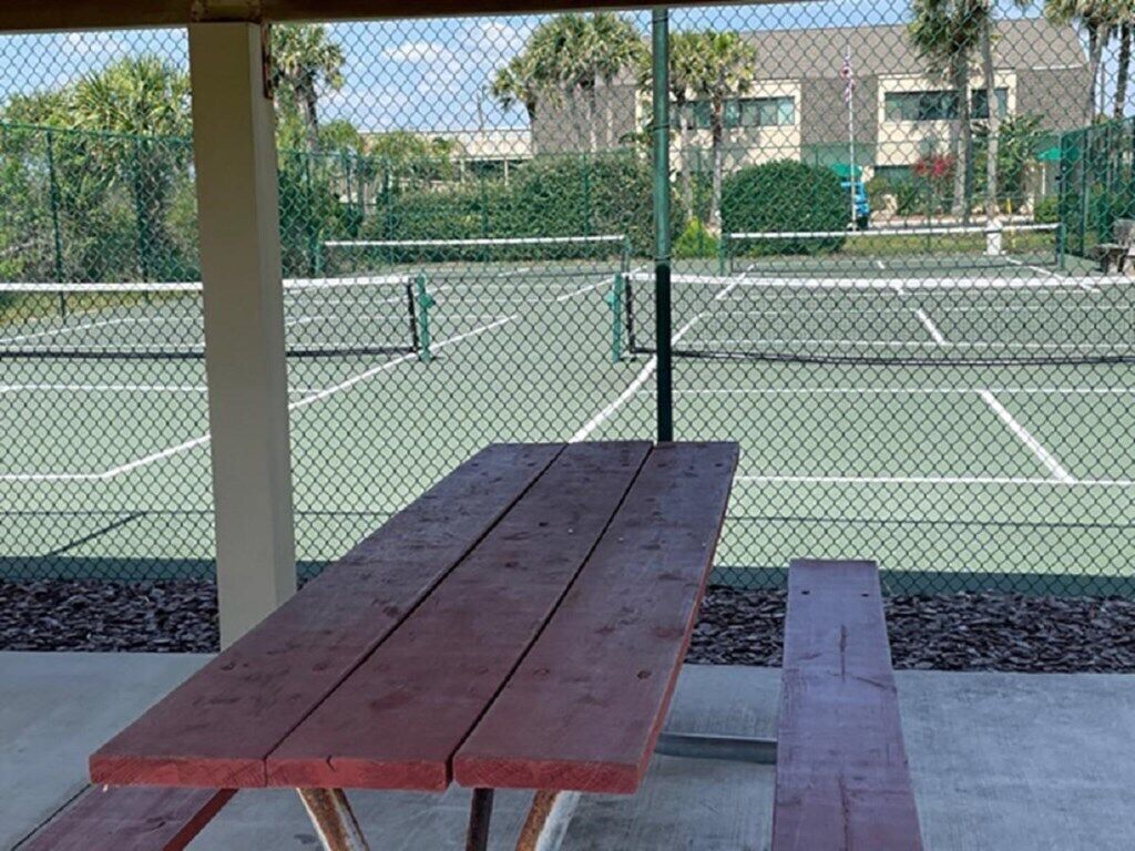 An outdoor tennis court with a picnic table in the foreground.